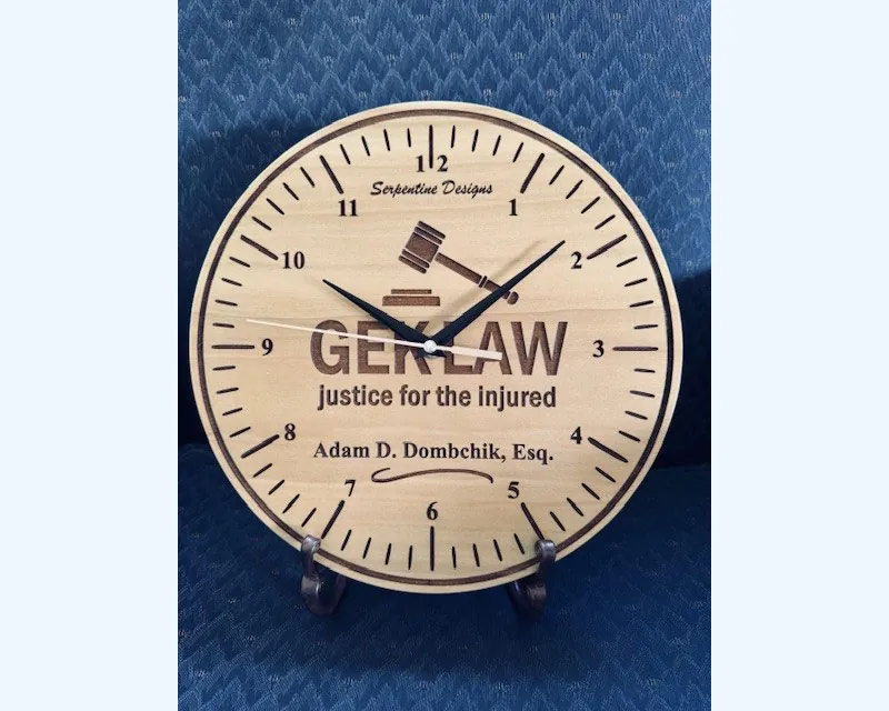 Handcrafted wooden clock gifted to GEKLaw by Sergeant Rene Sapien, featuring the GEKLaw logo, a gavel design, and the phrase "justice for the injured" with the name Adam D. Dombchik, Esq., engraved.