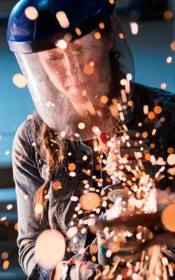 Female metalworker in protective gear grinding metal, sparks flying — representing GEKLAW’s commitment to protecting injured workers in high-risk occupations.