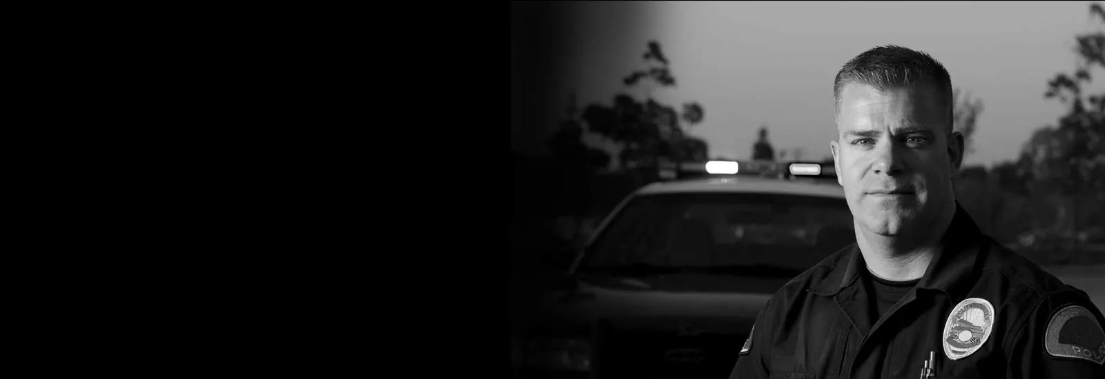 Police officer standing in front of a patrol car at dusk — representing GEKLAW’s commitment to protecting California’s law enforcement officers injured in the line of duty.